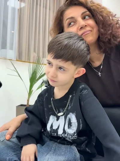 A boy after his haircut, sitting with the stylist who cut it.